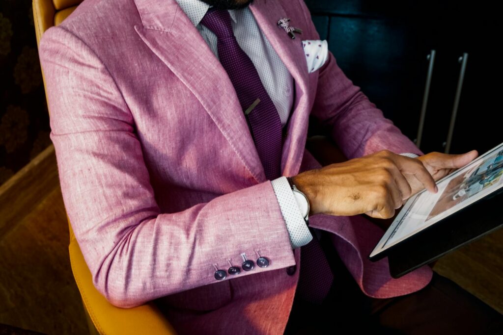 A fashionable businessman in a pink suit uses a tablet in a modern office setting.