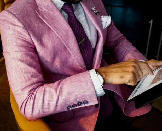 A fashionable businessman in a pink suit uses a tablet in a modern office setting.