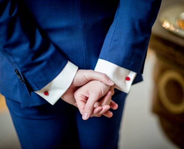 Close-up of an adult in a blue suit with hands crossed, showcasing elegance and business style.