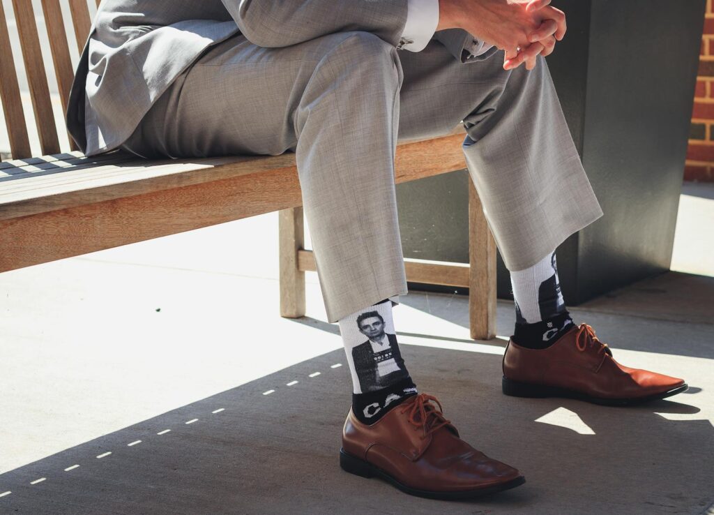 Businessman sits on bench in a grey suit showing personality with unique socks.