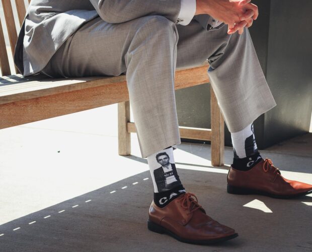 Businessman sits on bench in a grey suit showing personality with unique socks.