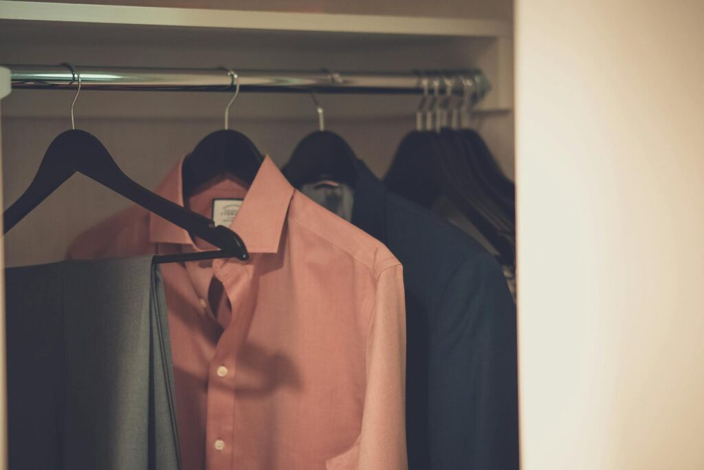 Stylish men's wardrobe featuring a formal suit and pink dress shirt neatly hung on hangers.