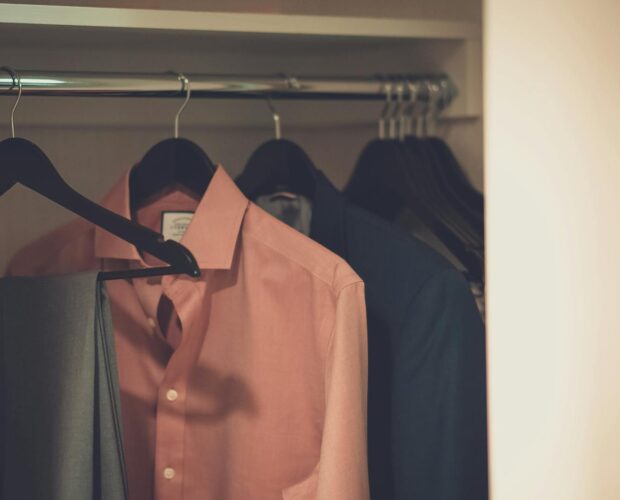 Stylish men's wardrobe featuring a formal suit and pink dress shirt neatly hung on hangers.