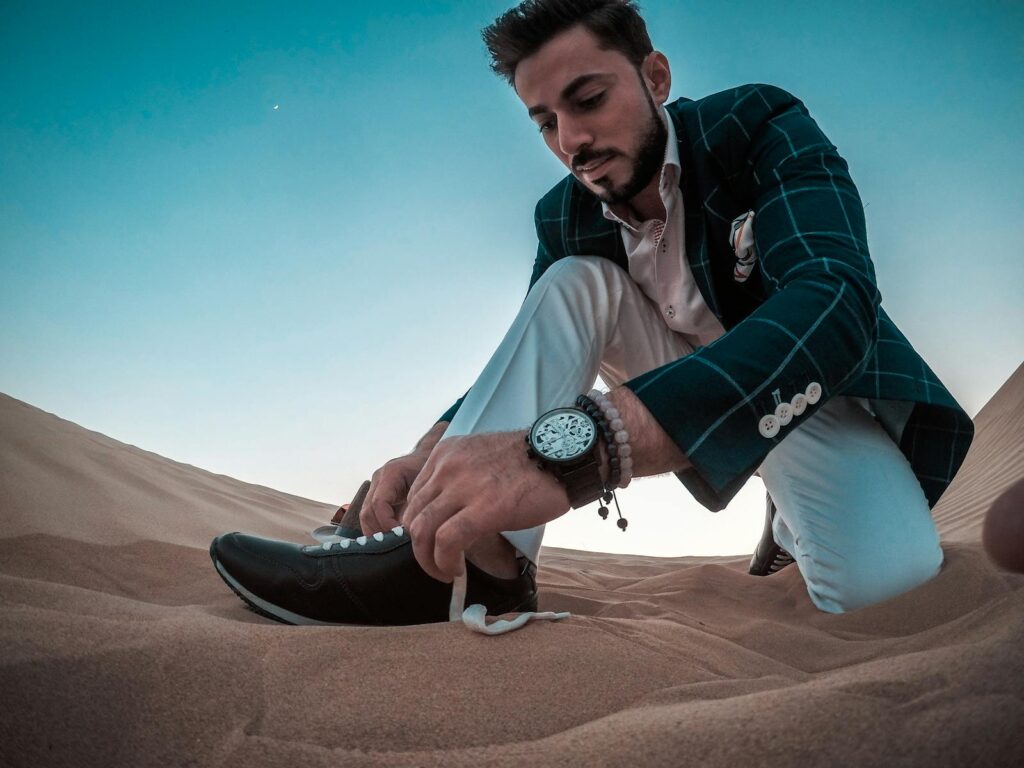 Stylish man tying sneakers in the Dubai desert. Captured at daytime showcasing fashion and lifestyle.