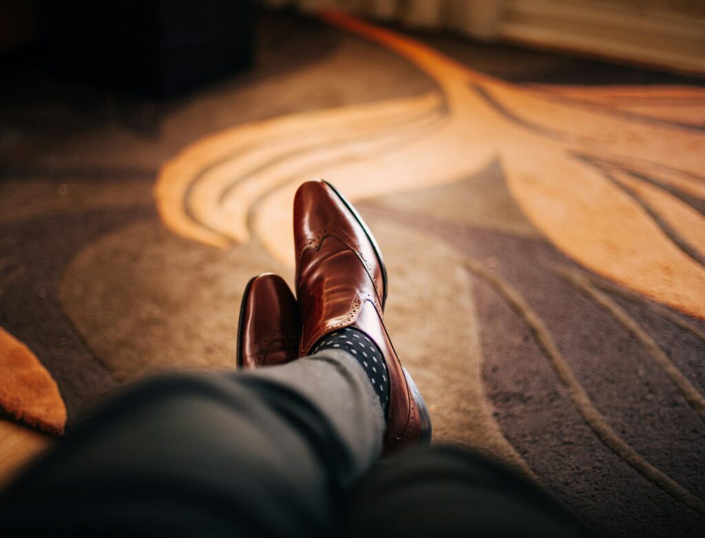 Close-up of polished brown leather shoes worn with patterned socks, relaxed indoors.