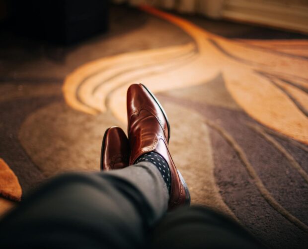 Close-up of polished brown leather shoes worn with patterned socks, relaxed indoors.