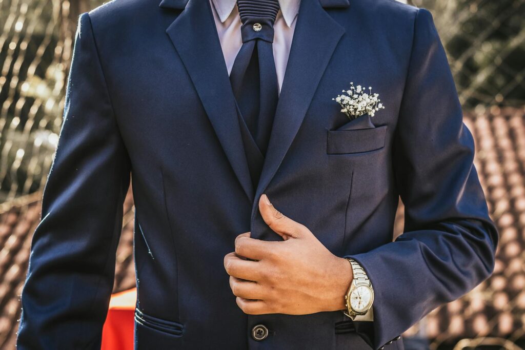 Adult man in a navy suit adjusting his tie, showcasing formal elegance outdoors.