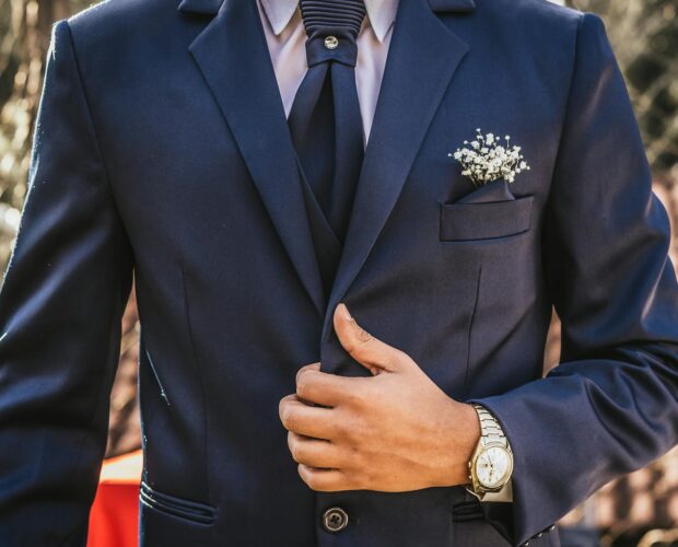 Adult man in a navy suit adjusting his tie, showcasing formal elegance outdoors.