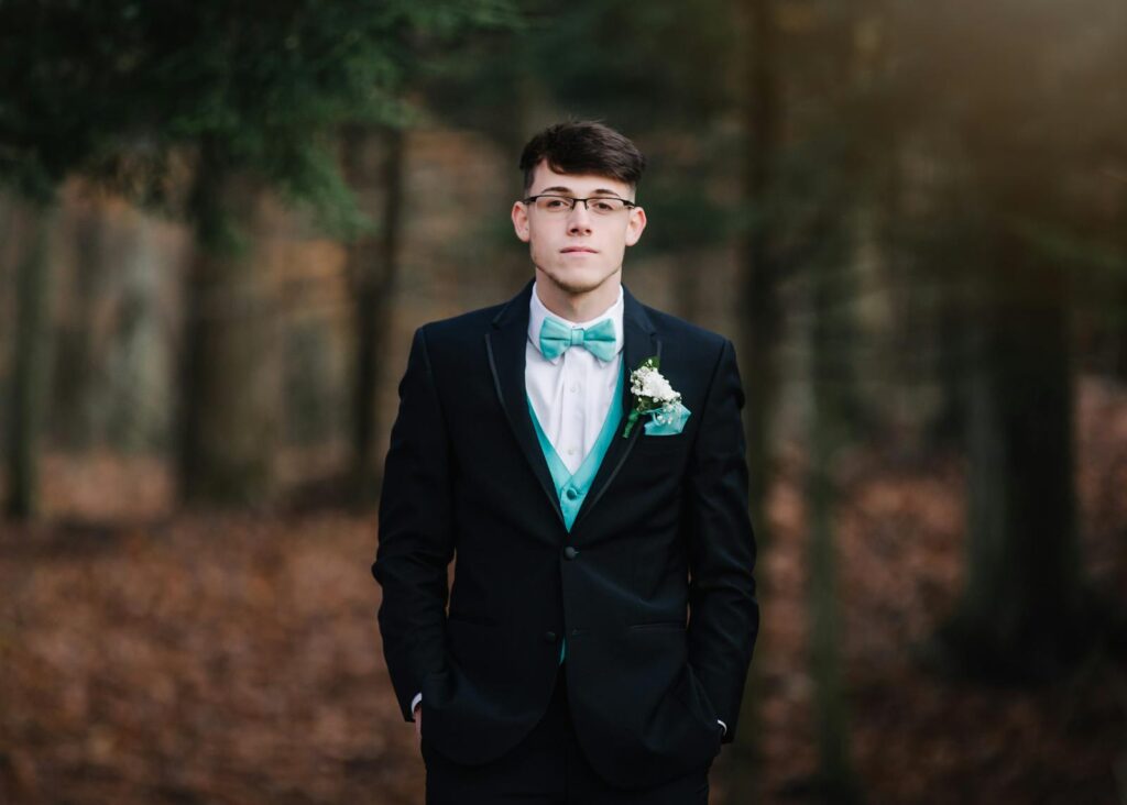 Young man in a sharp suit posing in a forest during the fall season.