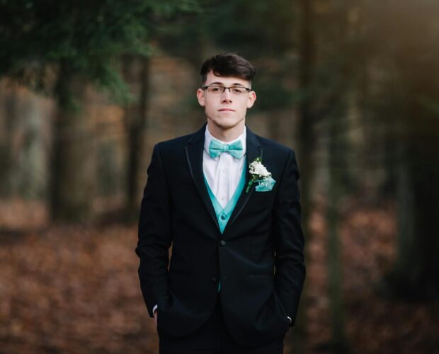 Young man in a sharp suit posing in a forest during the fall season.