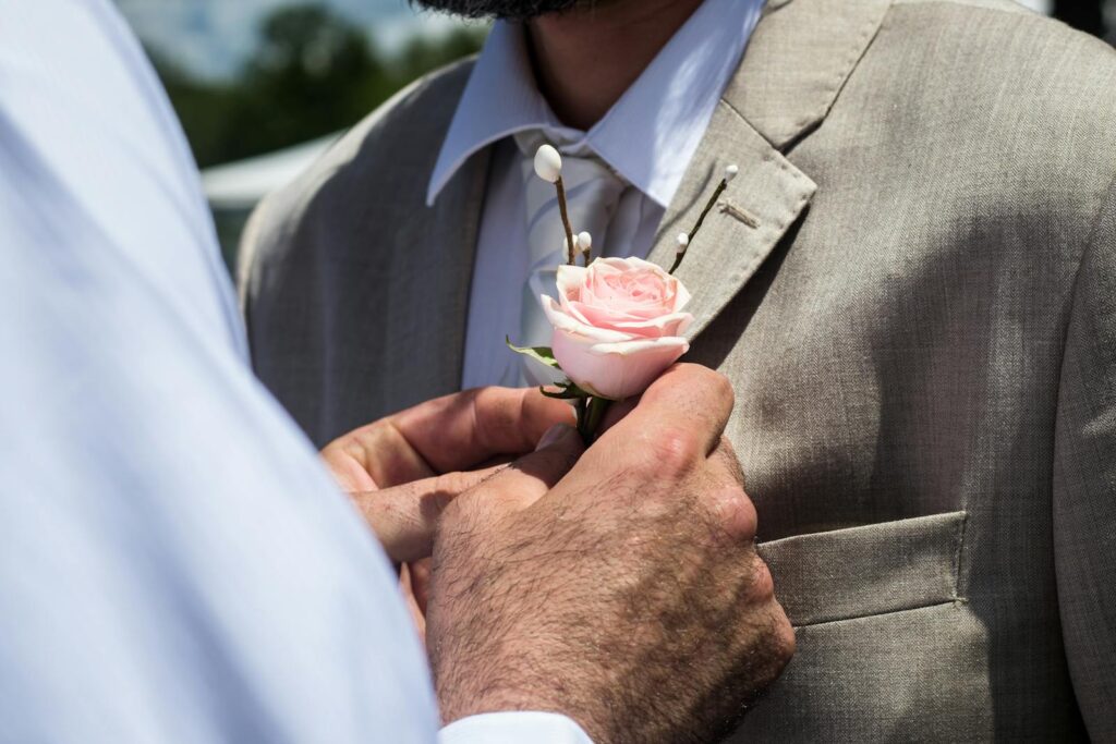 Close-up of a boutonniere being placed on a man's suit jacket.