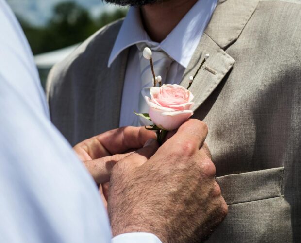 Close-up of a boutonniere being placed on a man's suit jacket.